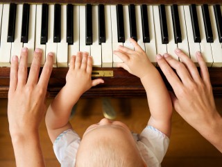 Closeup portrait of a baby learning to play piano with mother - from above